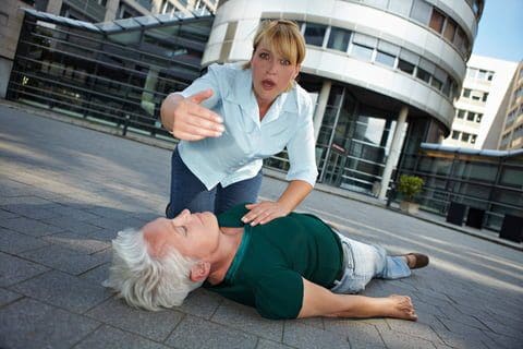 A woman performing CPR on a person lying on the ground in an outdoor setting.