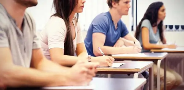 Group of students seated at desks in a classroom, focused on taking notes during a session.