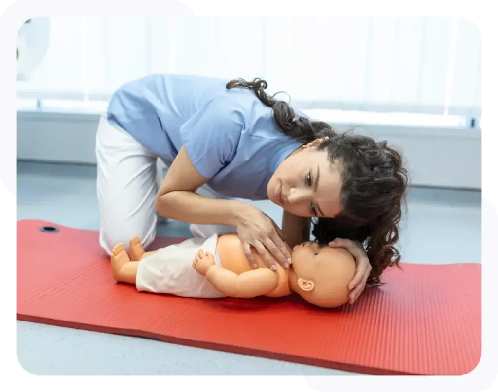 A person performing CPR on an infant manikin on a red mat in a training environment.